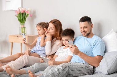 Evdeki yatak odasında modern aletlerle mutlu bir aile.