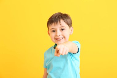Mutlu gülümseyen küçük çocuk arka plandaki izleyiciyi işaret ediyor.