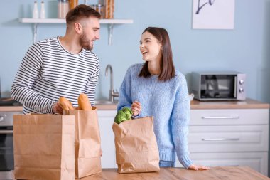Genç çift mutfaktaki marketten taze ürünleri indiriyor.