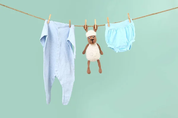 Baby clothes with toy hanging on rope against color background