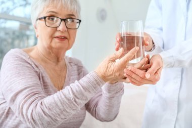 Parkinson sendromlu yaşlı bir kadına klinikte su içiren kadın doktor.