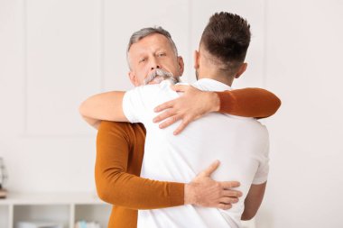 Büyük adam ve yetişkin oğlu evde sarılıyorlar.