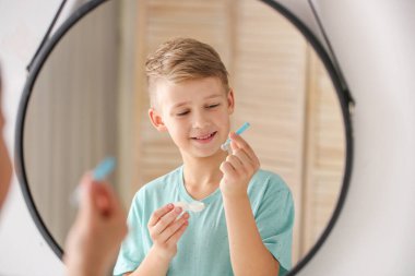 Little boy with contact lens case and tweezers near mirror at home clipart