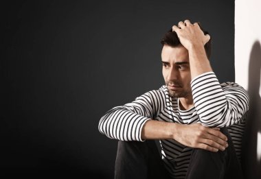 Depresyondaki genç adam duvarın yanında oturuyor.