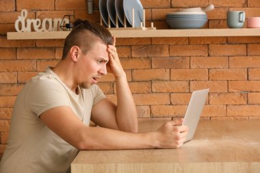 Mutfakta dizüstü bilgisayarı olan endişeli bir genç adam.