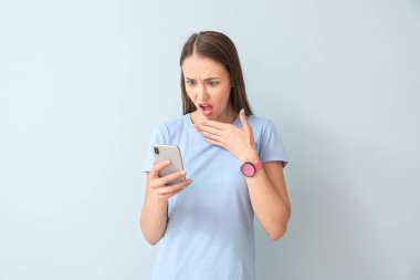 Şok olmuş genç bir kadın ve renkli bir cep telefonu.
