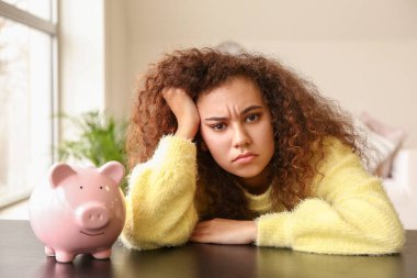 Evinde domuz kumbarası olan üzgün bir Afro-Amerikalı kadın.