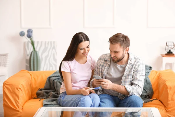 Young couple with pregnancy test and mobile phone at home