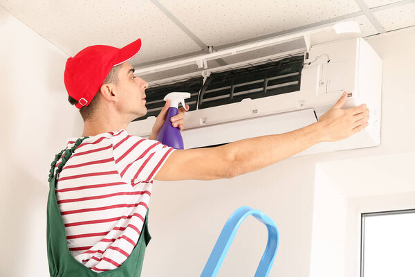 Male technician cleaning air conditioner indoors