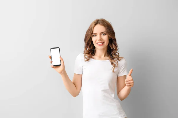 Mladá Žena Mobilním Telefonem Ukazující Palec Nahoru Světlém Pozadí — Stock fotografie