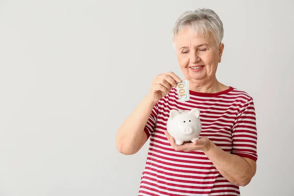 Senior Woman Putting Money Piggy Bank Light Background — Stock Photo, Image