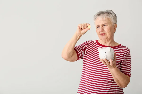 Mulher Sênior Pensativo Com Banco Porquinho Dinheiro Fundo Leve — Fotografia de Stock