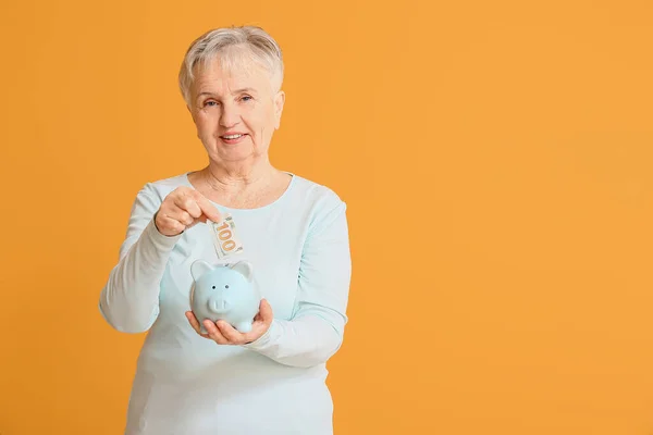 老年妇女把钱存进储蓄罐的背景是彩色的 — 图库照片