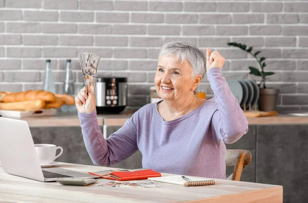Happy senior woman with money at home