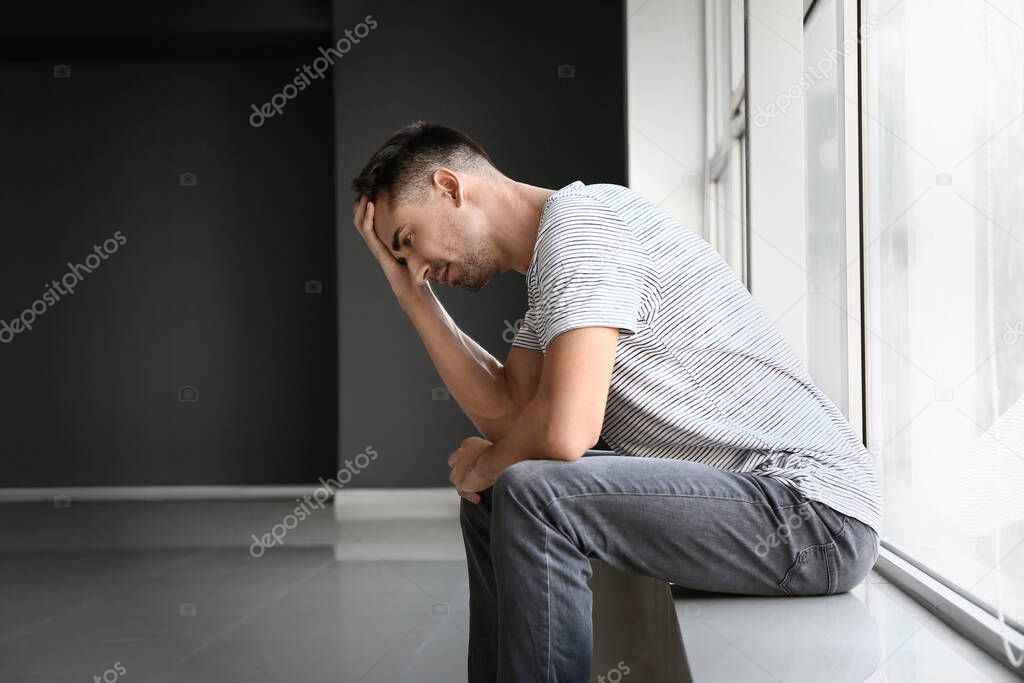 Depressed young man near window