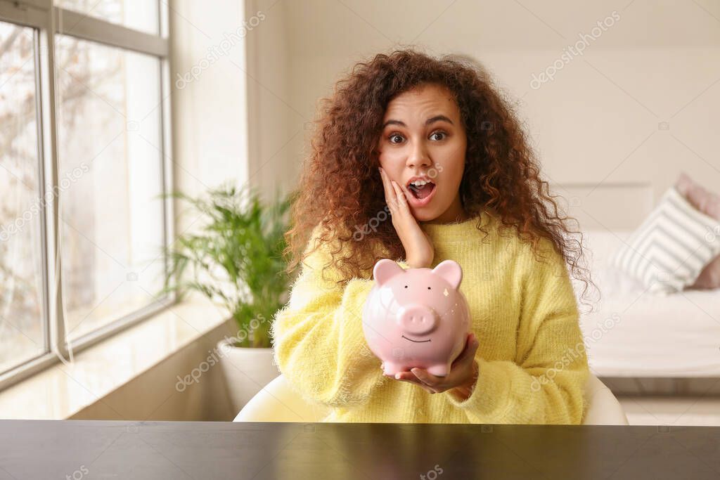 Surprised African-American woman with piggy bank at home