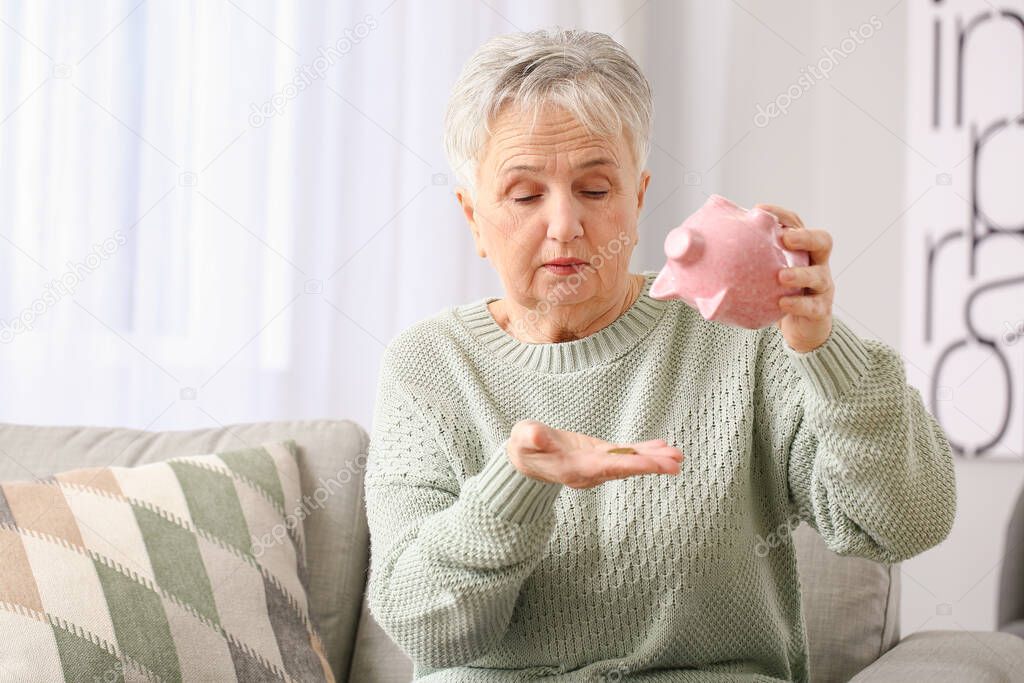 Sad senior woman with empty piggy bank at home