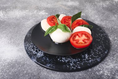 Domatesli Mozzarella peyniri ve gri arka planda fesleğen.