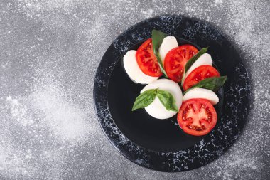 Domatesli Mozzarella peyniri ve gri arka planda fesleğen.