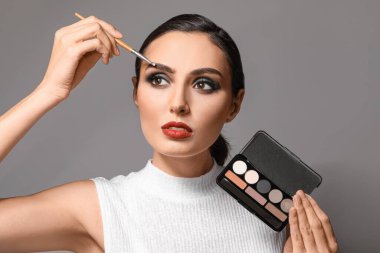 Gri arka plana makyaj yapan güzel bir genç kadın.