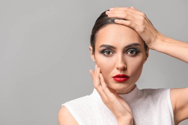Gri arka planda güzel makyajlı genç bir kadın.