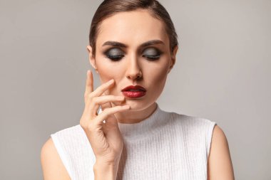 Gri arka planda güzel makyajlı genç bir kadın.