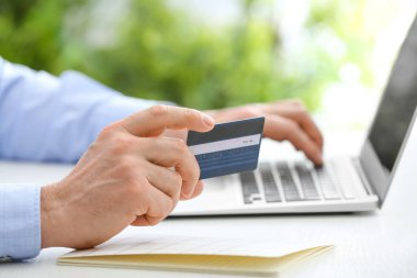 Masada dizüstü bilgisayarı ve kredi kartı olan adam, yakın plan.