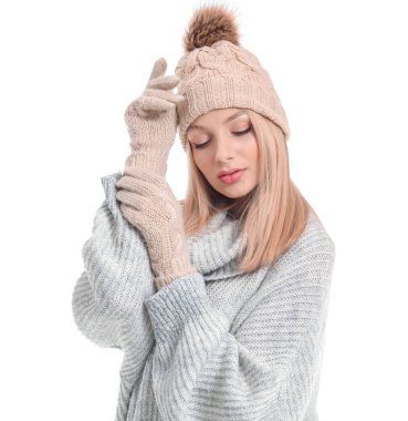 Beyaz arka planda kalın kazaklı, şapkalı ve eldivenli genç bir kadın.