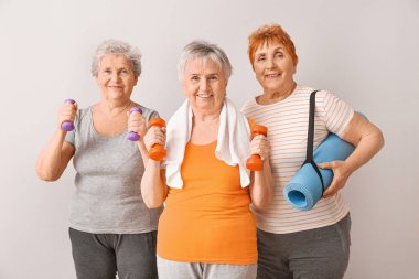 Hafif arka planda spor aletleri olan yaşlı kadınlar