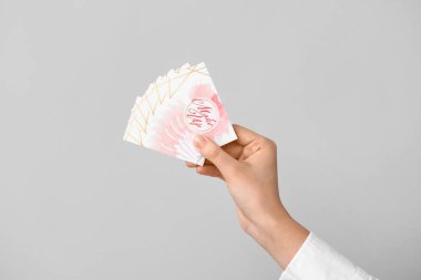 Gri arkaplanda makyaj sanatçılarının kartvizitleri olan bir kadın eli.