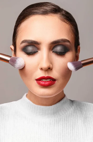 Hermosa Joven Con Pinceles Maquillaje Sobre Fondo Gris — Foto de Stock