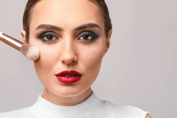 Bella Giovane Donna Che Applica Trucco Sullo Sfondo Grigio — Foto Stock