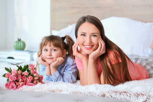 Little girl and her mother with flowers in bedroom