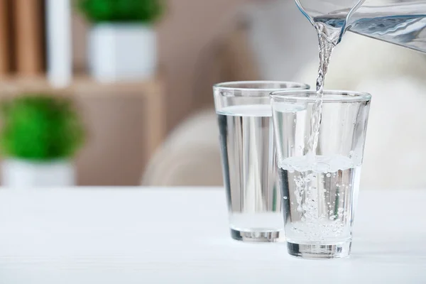 部屋のテーブルの上のガラスに新鮮な水を注ぐ — ストック写真