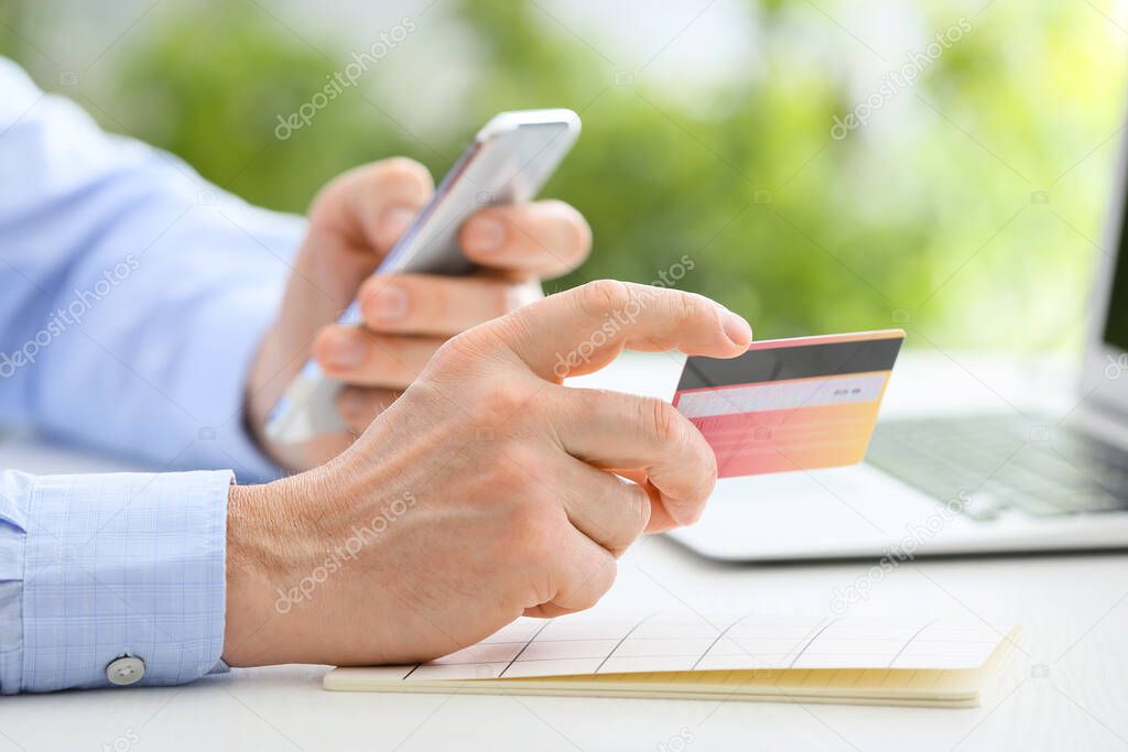 Man with mobile phone and credit card at table, closeup