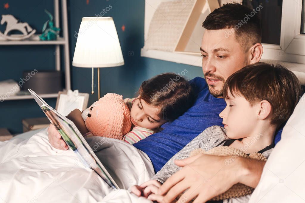 Father reading bedtime story to his little children at home