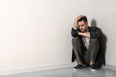 Depresyondaki genç adam ışık duvarının yanında oturuyor.