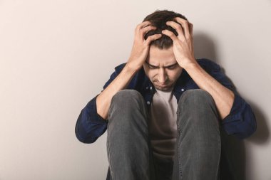 Depresyondaki genç adam ışık duvarının yanında oturuyor.