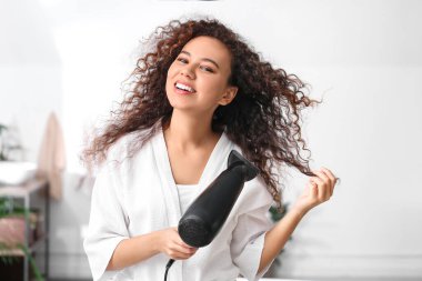 Evde saç kurutma makinesi olan güzel bir Afro-Amerikalı kadın.