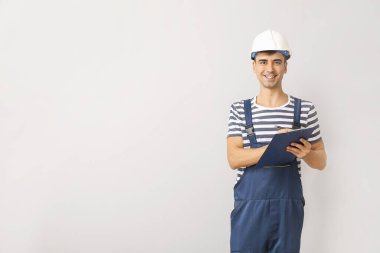 Handsome male worker with clipboard on light background