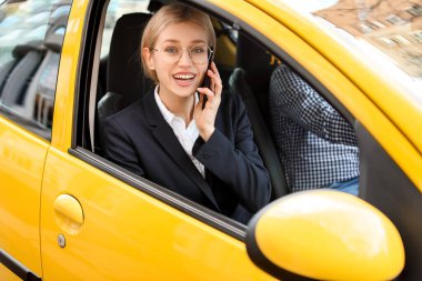 Genç iş kadını takside otururken telefonla konuşuyor.