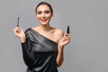 Gri arka plana makyaj yapan güzel bir genç kadın.