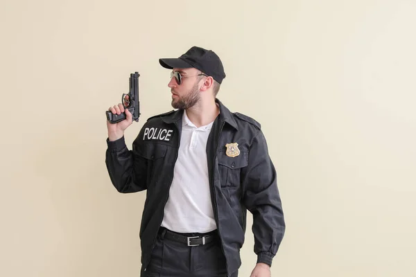 Male police officer with gun on light background