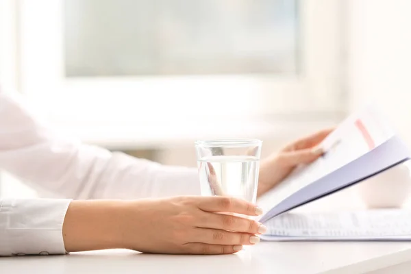 テーブルで新聞を読みながら水を飲む女 — ストック写真