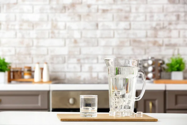 Glass and jug of cold clean water on table in kitchen