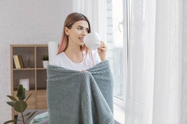 Pencerenin yanında bir fincan çayı olan güzel genç bir kadın.