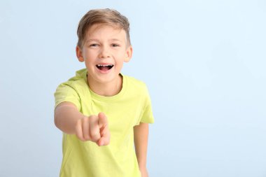 Küçük mutlu çocuk beyaz arka plandaki izleyiciyi işaret ediyor.