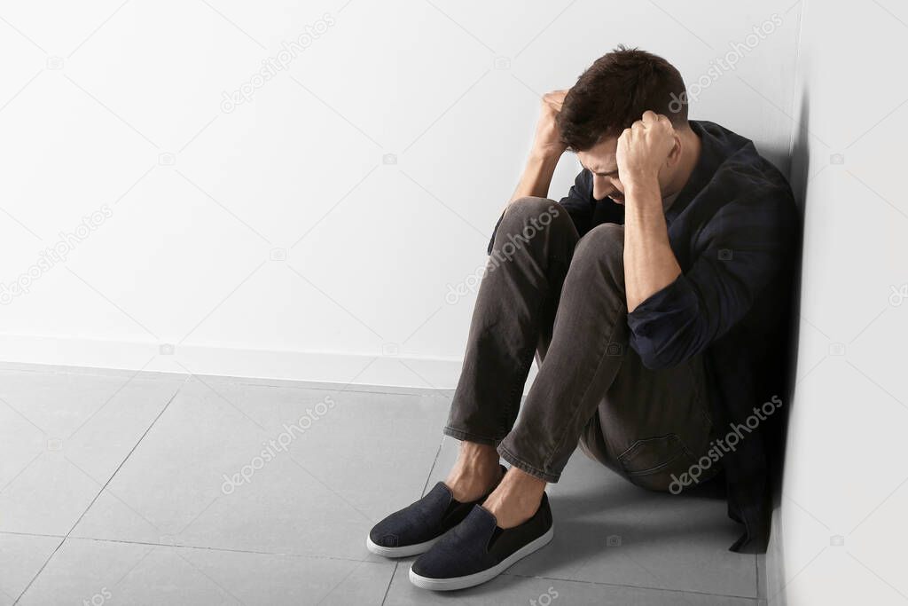 Depressed young man sitting near light wall