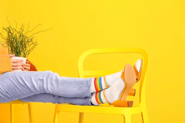 Legs of young woman in socks and sandals on chair against color background