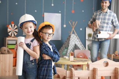 İnşaatçı gibi giyinmiş küçük çocuklar evlerinde sökülmüş evlerle oynuyorlar.